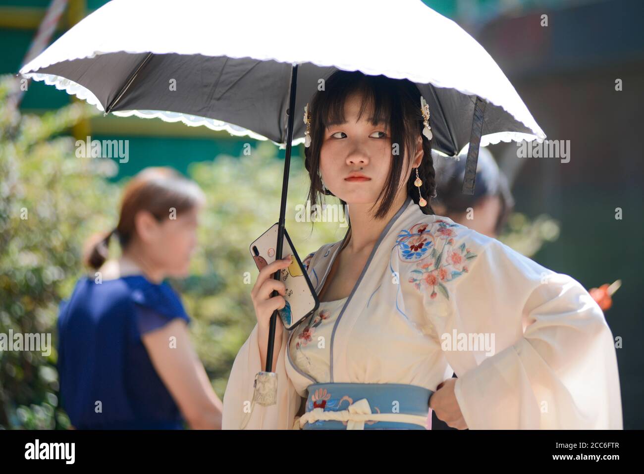 Ein chinesisches junges Mädchen, das mit traditioneller Kleidung und Regenschirm gekleidet ist und ihr Handy hält. Jianghan Road, Wuhan, China Stockfoto