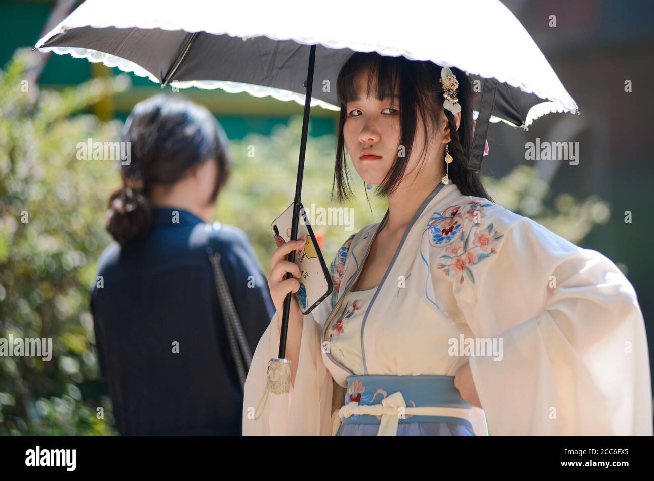 Ein chinesisches junges Mädchen, das mit traditioneller Kleidung und Regenschirm gekleidet ist und ihr Handy hält. Jianghan Road, Wuhan, China Stockfoto