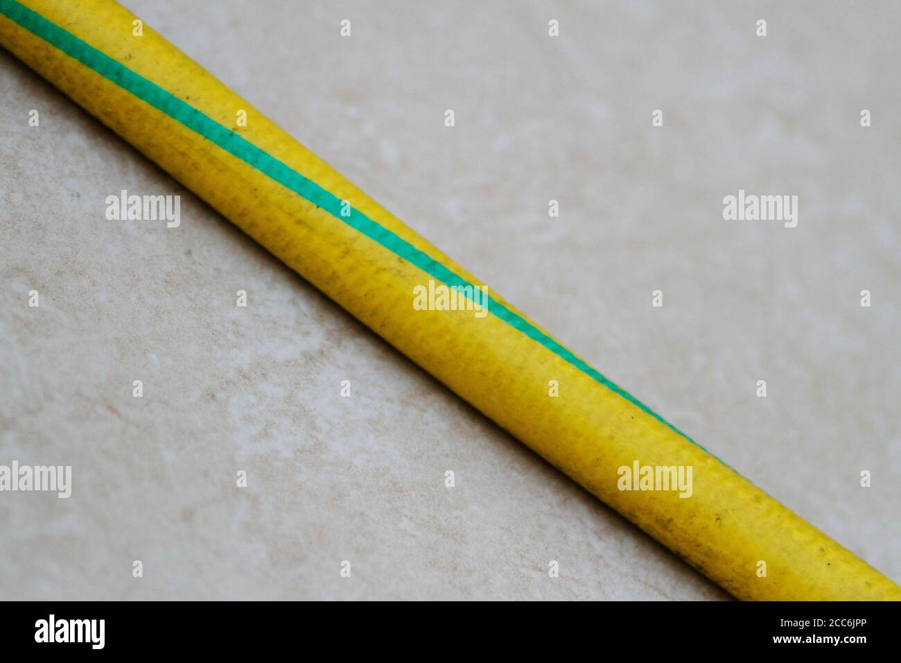 Gelb und grün gefärbter alter Schlauch auf dem Boden. Gelber und grüner alter Schlauch. Alte Gartenschlauch Nahaufnahme. Stockfoto