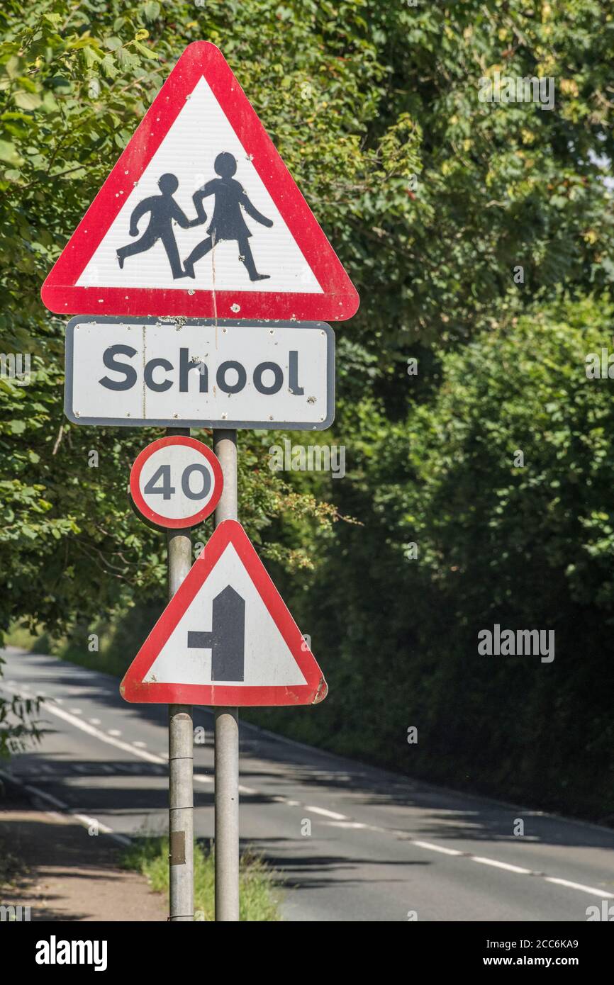 Ländliche Land Schule dreieckiges Warnschild in Straßenhecke. UK Junge und Mädchen zu Fuß Piktogramm für Sicherheitsbewusstsein. Metapher zurück in die Schule. Stockfoto
