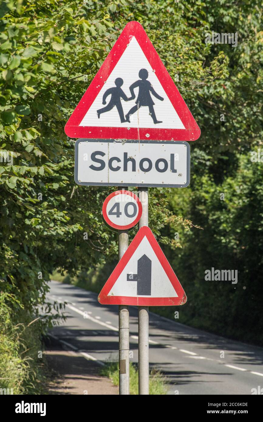 Ländliche Land Schule dreieckiges Warnschild in Straßenhecke. UK Junge und Mädchen zu Fuß Piktogramm für Sicherheitsbewusstsein. Metapher zurück in die Schule. Stockfoto