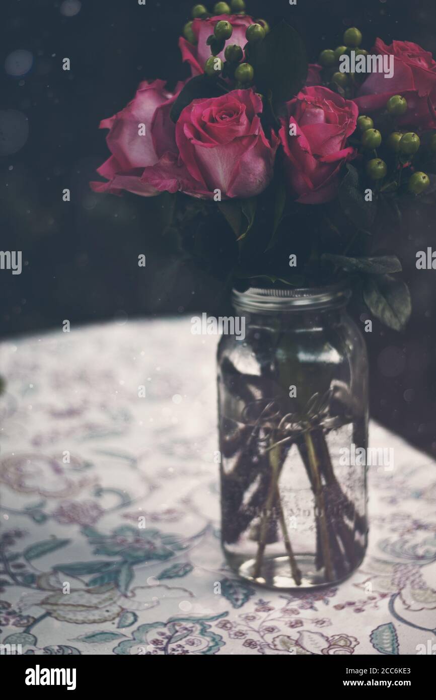 Bouquet von rosa Rosen in Mason Jar auf gemusterter Tischdecke Stockfoto