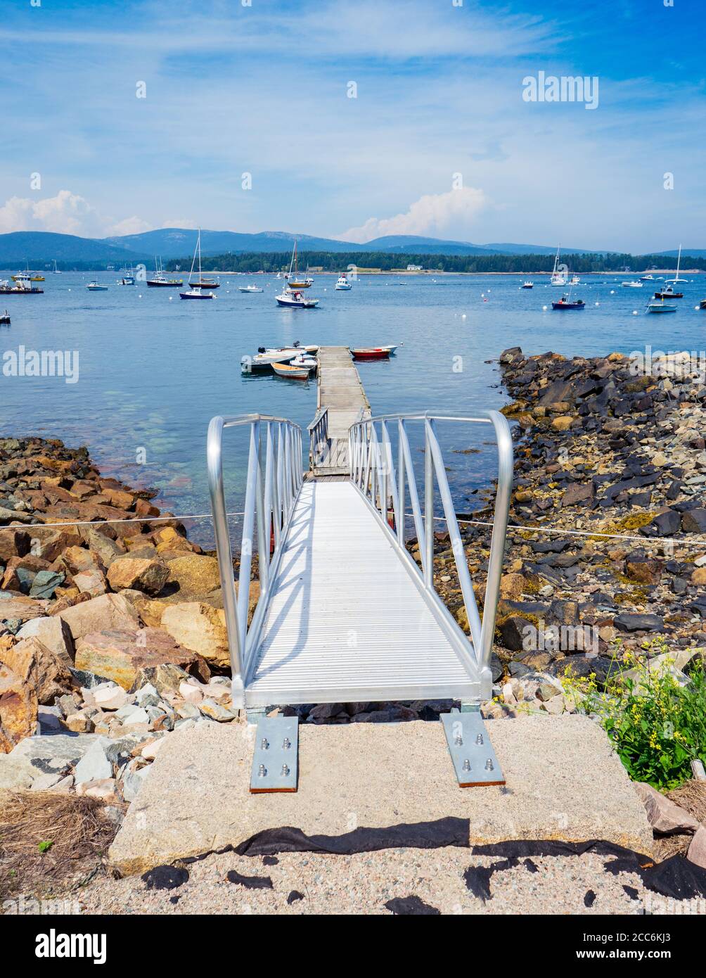 Eine Bootsrampe führt hinunter zu einem Dock in Southwest Harbor in Maine. Es gibt mehrere Arten von Booten, die an einem schönen Sommertag im Hafen festgemacht sind. Stockfoto