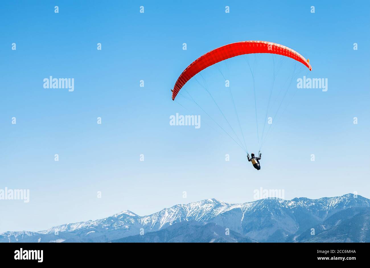 Sportler auf rotem Gleitschirm, der über die schneebedeckten Berggipfel schweben Stockfoto