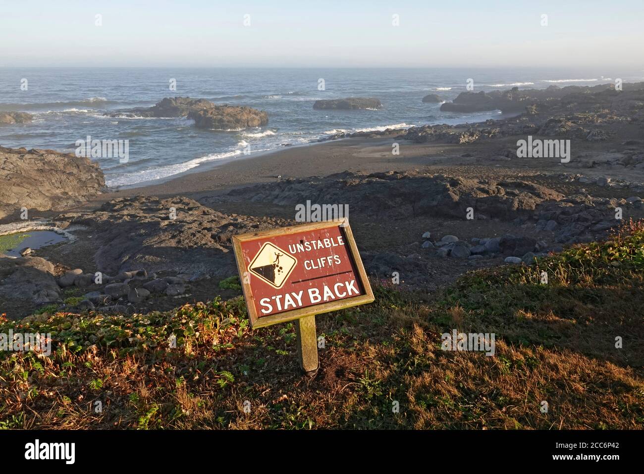 Ein Schild warnt Besucher und Wanderer vor steilen Klippen auf einem Küstenweg entlang der Pazifikküste von Oregon in der Nähe der Stadt Yachats, Oregon. Stockfoto
