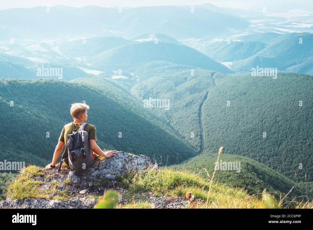 Junger Mann Tourist Backpacker sitzt auf dem Hügel mit Wunderschönes Talpanorama Stockfoto