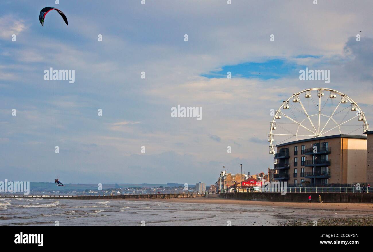 Portobello, Edinburgh, Schottland, Großbritannien. 19. August 2020. Windiger Nachmittag blies den Dunst weg, der am Morgen mit verstreuten Sonnenstrahlen später anhielt. Wind 22 km/h mit möglichen Böen von 42 km/h, die diesem Kite Surfer helfen, ein paar Airs zu bekommen. Im Bild: Rechts das rotuntant Riesenrad, das sich nicht gedreht hat, da es keine Lizenz zum Bedienen hat. Stockfoto