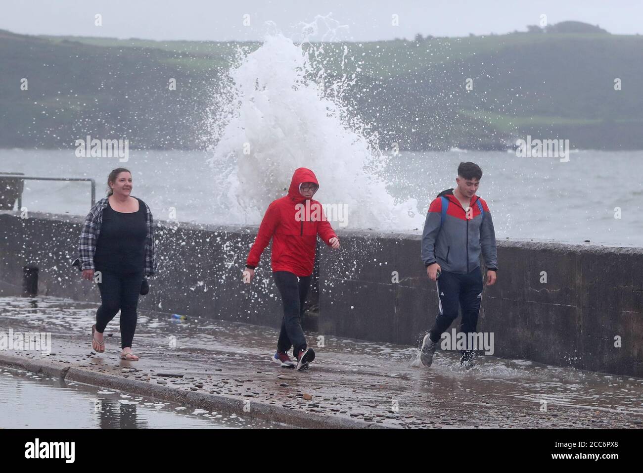 Die Leute laufen vorbei, als die Wellen am Front Strand in Youghal, Co. Cork, krachen. Met Eireann hat eine rote Windwarnung für die Region herausgegeben, und eine orange Warnung wurde für Galway, Mayo, Clare, Kerry, Limerick und Waterford ausgegeben, während Sturm Ellen von Mittwoch Abend über das Land fegt. Stockfoto