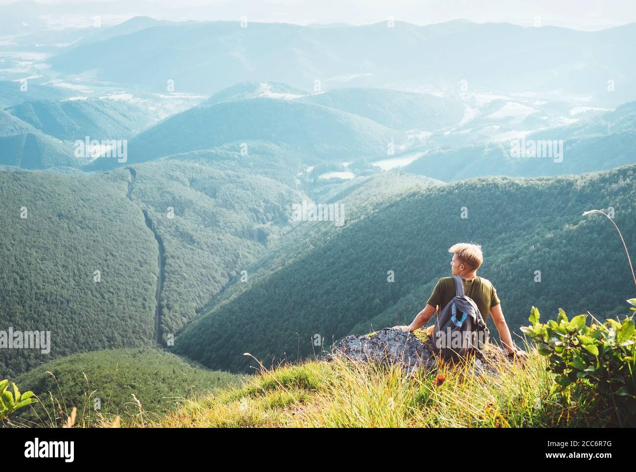 Junger Mann Tourist sitzt auf dem Hügel mit schönen Talpanorama Stockfoto