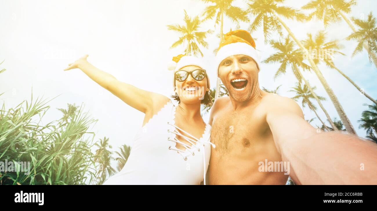 Glücklich lächelndes Paar machen Selfie-Foto in Santa Hüte unter den Palmen. Tropischer Neujahrsurlaub Stockfoto
