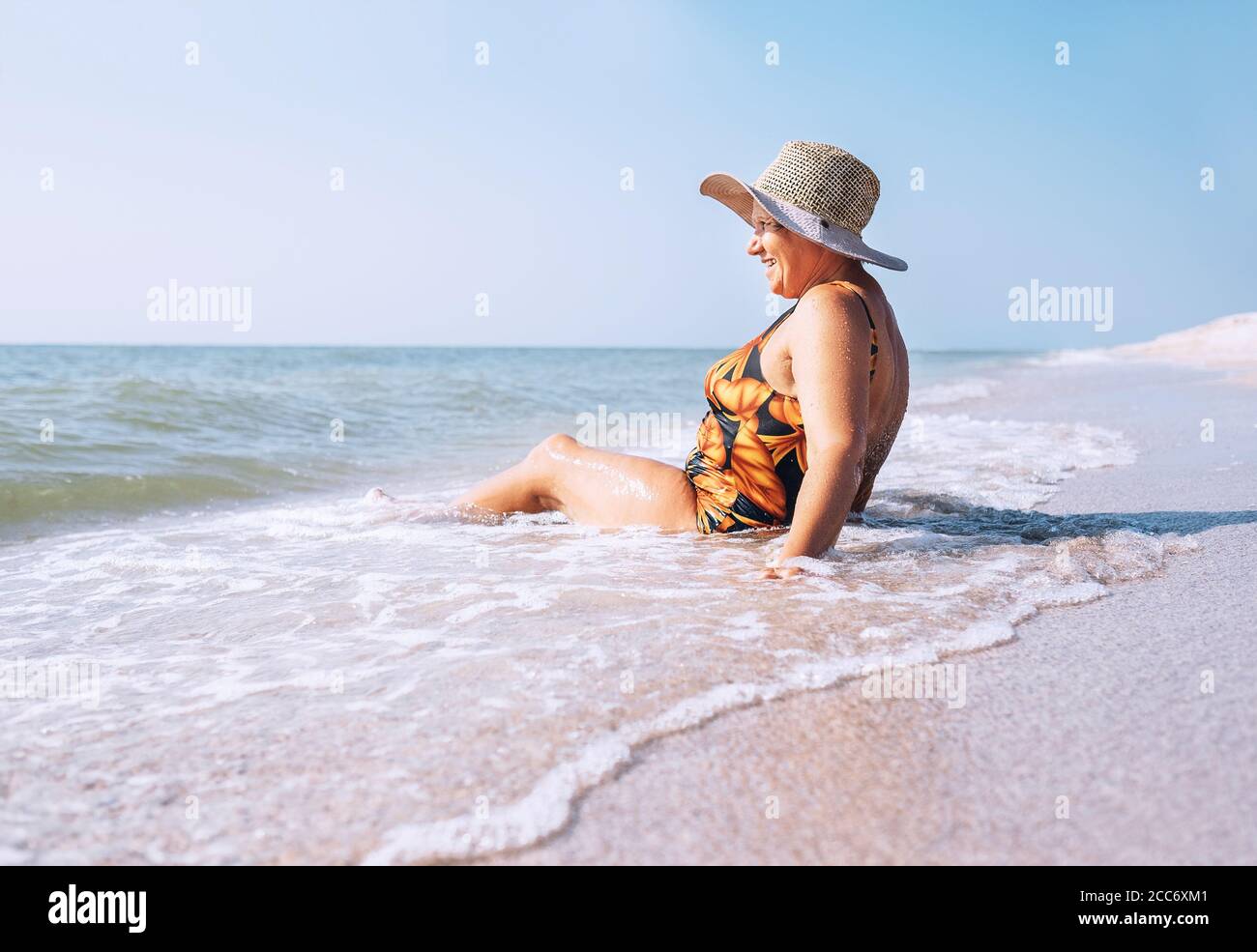 Ältere Frau genießen Strandurlaub sitzen auf dem Meer surfline Stockfoto