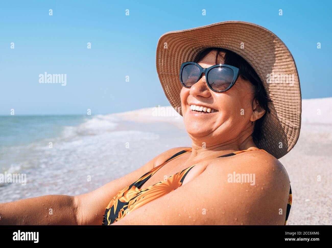 Glücklich lächelnd ältere Frau in Sonnenbrille und großen Hut Sonnenbaden am Meer Stockfoto