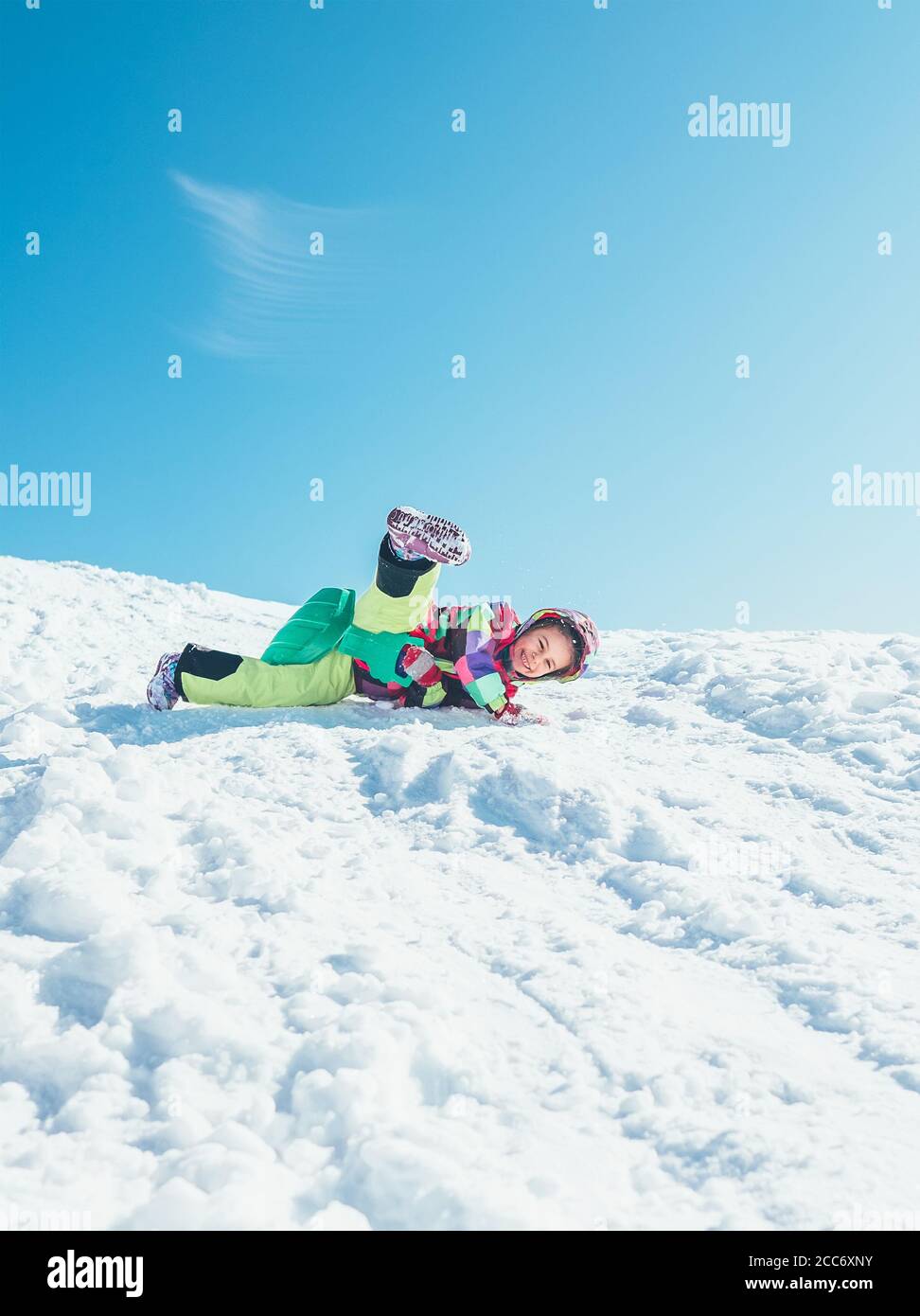 Kleine Mädchen haben Spaß, wenn Rutschen vom Schneehügel. Sie lächelt glücklich und fällt von ihrem Schlitten herunter Stockfoto