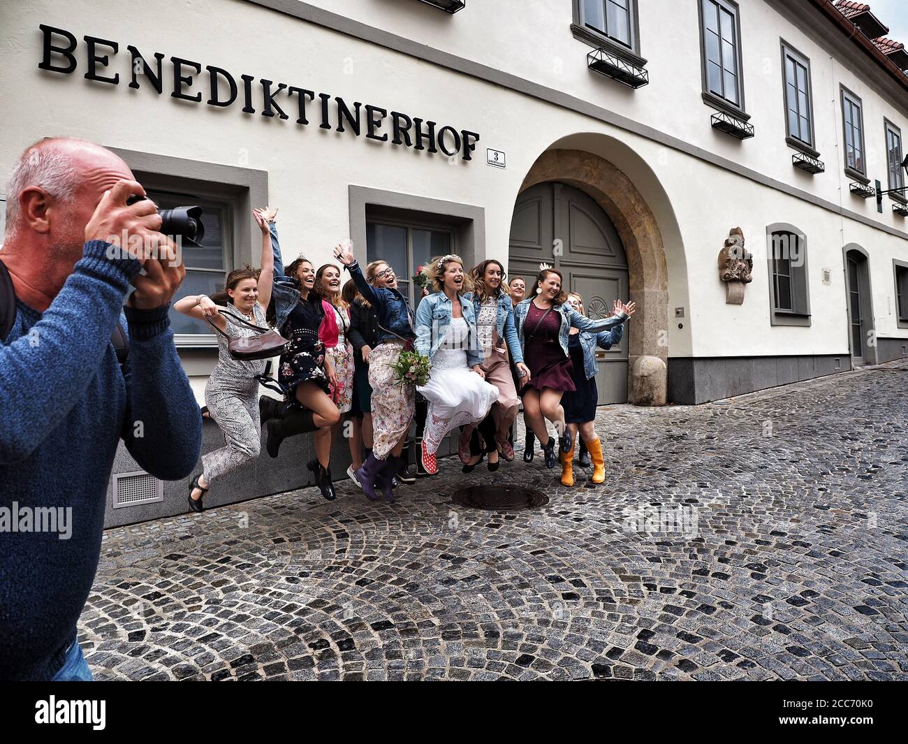 GUMPOLDSKIRCHEN, ÖSTERREICH - 09/01/2018. Glückliche kaukasische Braut mit Brautjungfern, die auf der Straße springen. Hochzeit in Gummistiefeln an regnerischen Tagen. Stockfoto