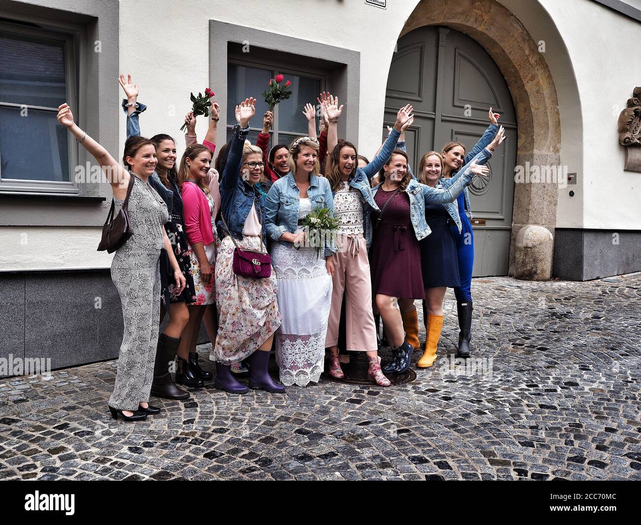 GUMPOLDSKIRCHEN, ÖSTERREICH - 09/01/2018. Glückliche kaukasische Braut mit Brautjungfern mit Händen auf der Straße. Hochzeit in Gummistiefeln an regnerischen Tagen. Stockfoto