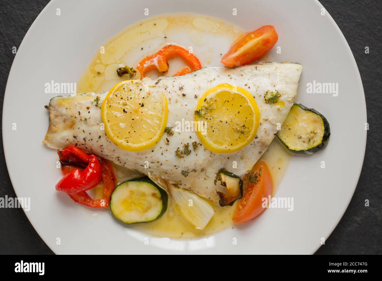 Ein Filet aus einer Linie gefangen wilden Bass, Dicentrarchus labrax, das mit Gemüse, Zitronenscheiben, Olivenöl und Butter geröstet und gewürzt w Stockfoto