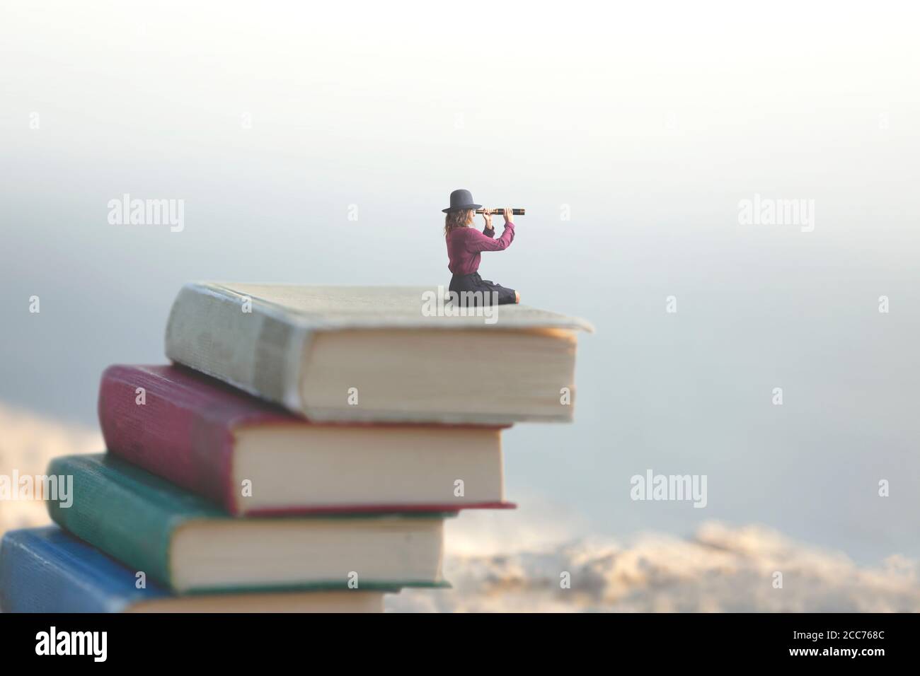 Miniatur Frau schaut auf die Unendlichkeit mit dem Spyglass auf Eine Skala von Büchern Stockfoto