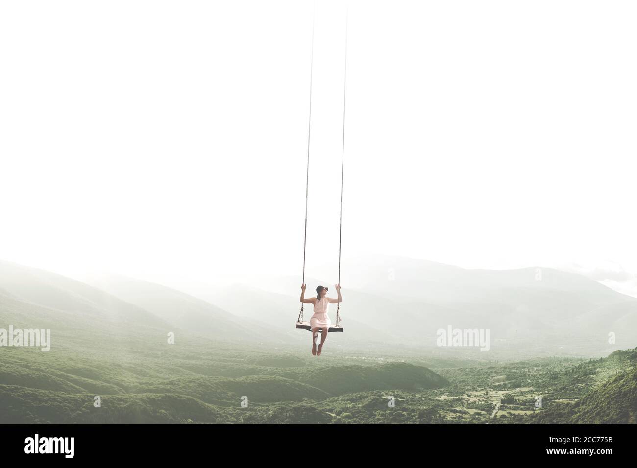 Surrealer Moment einer Frau, die Spaß auf einer Schaukel hat Am Himmel hängen Stockfoto