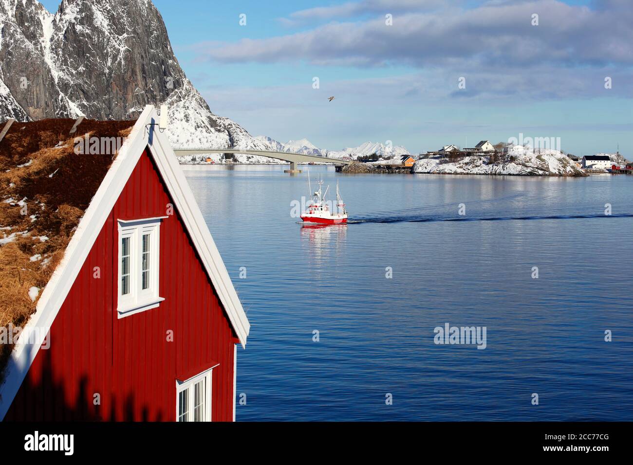 Schöne klassische Ansicht von Winter Fjord mit rotem Haus im Vordergrund und coming roten Fischerboot in Olenilsoya in reine, Lofoten Inseln, Norwegen Stockfoto