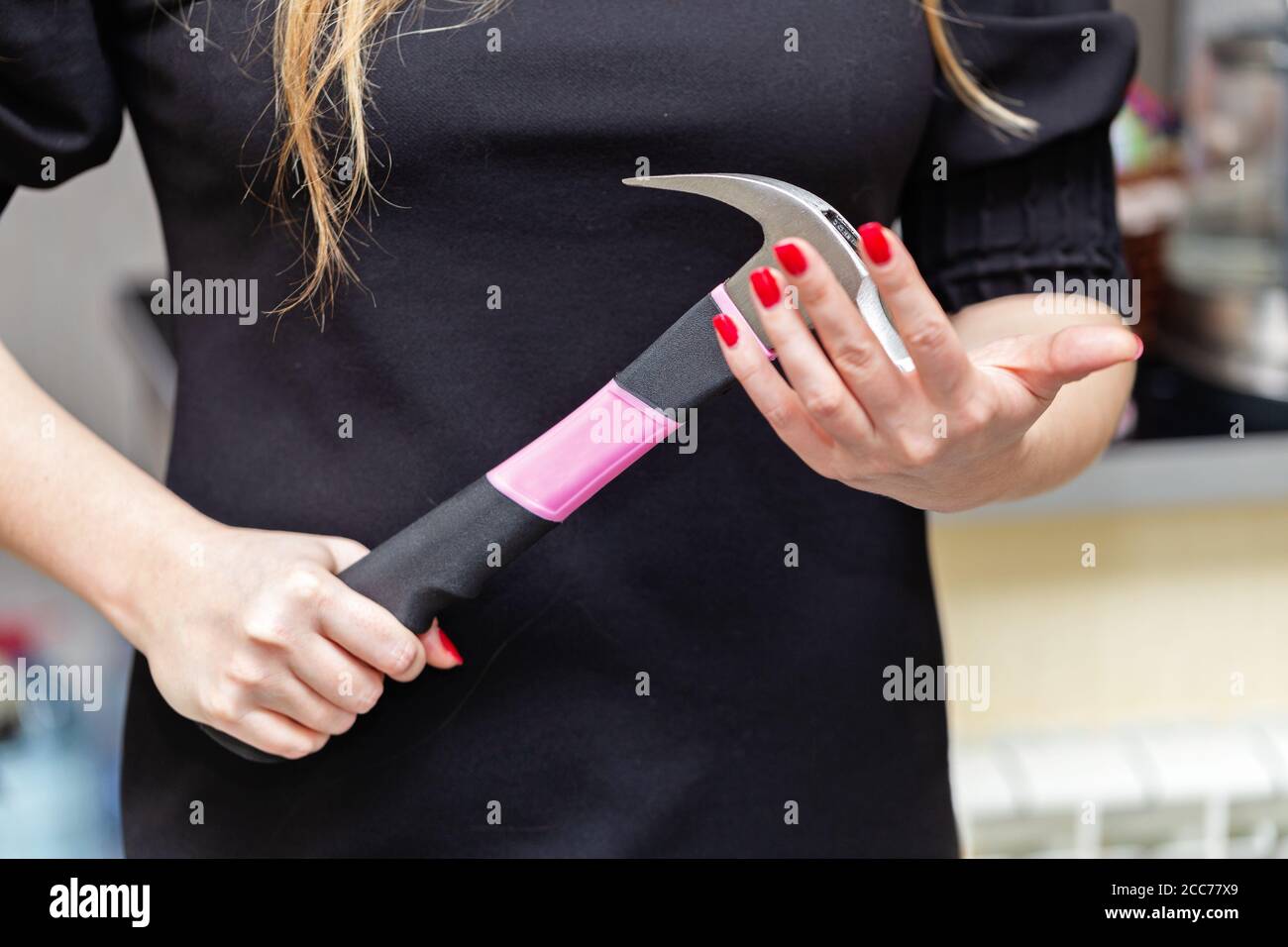 Frauenhände halten einen großen Hammer mit einem rosa Griff in einer bedrohlichen oder unentschlossenen Position. Stockfoto