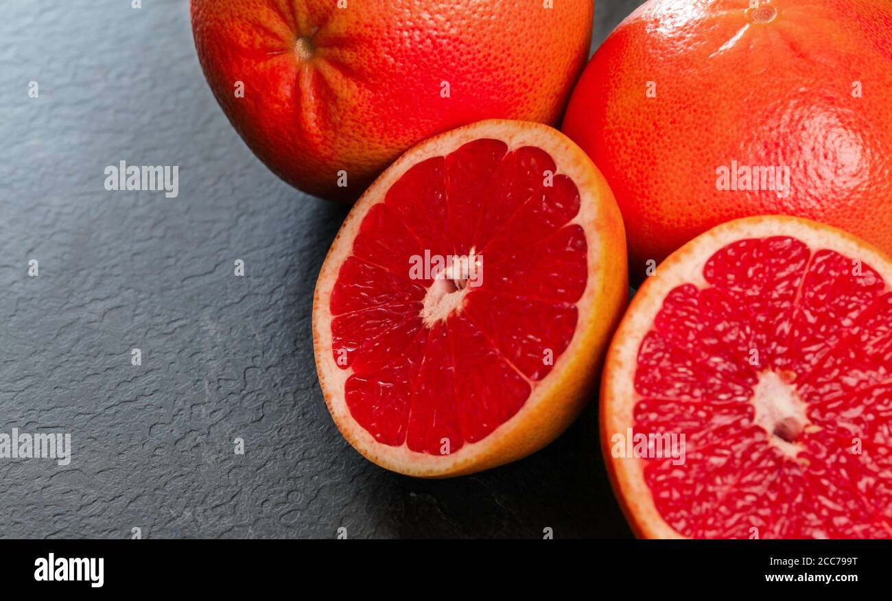 Rosa Grapefruits Hälften, ganze Zitrusfrüchte im Hintergrund, auf schwarzem schieferartigen Brett Stockfoto