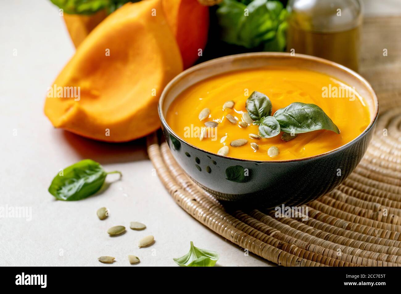 Schüssel mit vegetarischer Kürbis- oder Karotten-Sahnesuppe, dekoriert mit frischem Basilikum, Olivenöl und Kürbiskernen auf weißer Textur-Tabelle mit Zutaten oben. Stockfoto