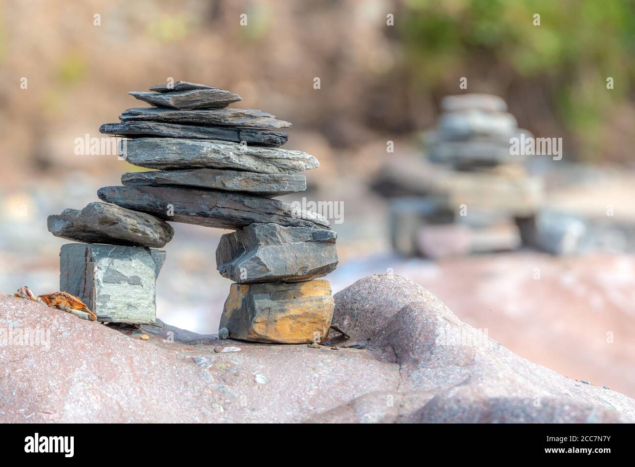 Ein kleiner inuksuk auf dem Felsen. Ein weiterer Inuksuk im Hintergrund, Außentefe des Feldes. Eine kleine Krabbe befindet sich neben dem Inuksuk. Stockfoto