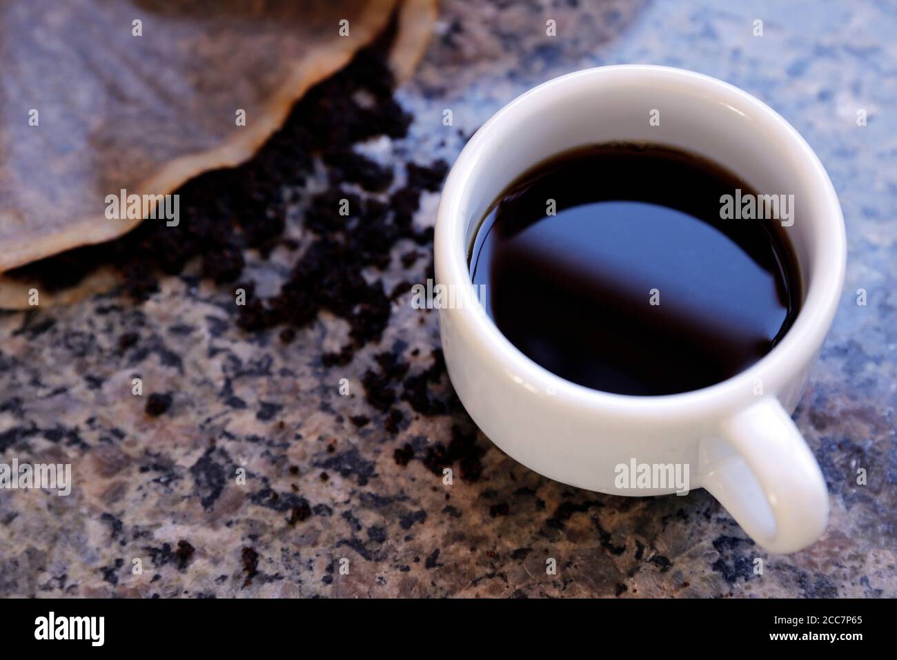 Tisch mit weißer Tasse Kaffee und gemahlenem Kaffeesatz Im Sieb Stockfoto