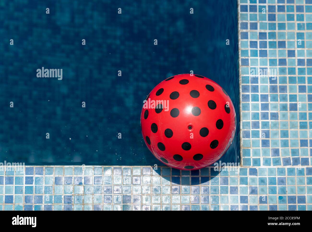 Draufsicht auf eine rote Kugel, die an einem sonnigen Tag an der Ecke eines Schwimmbades schwimmt. Stockfoto