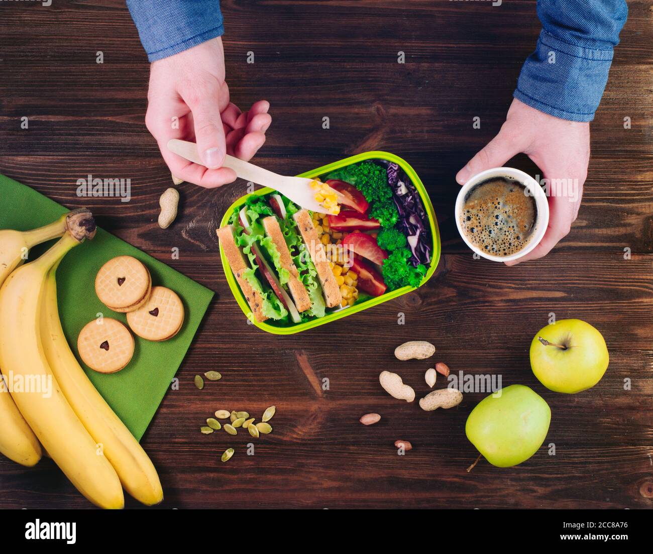 Männchen Hände essen sein Mittagessen von der Lunchbox auf rustikalem Holz Hintergrund Stockfoto