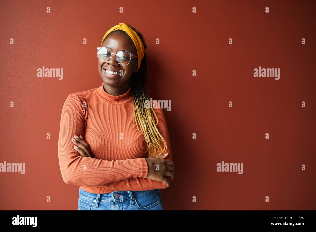 Portrait von African glückliche Frau mit stilvollen Frisur und in Brillen lächeln vor der Kamera, während sie vor dem braunen Hintergrund stehen Stockfoto