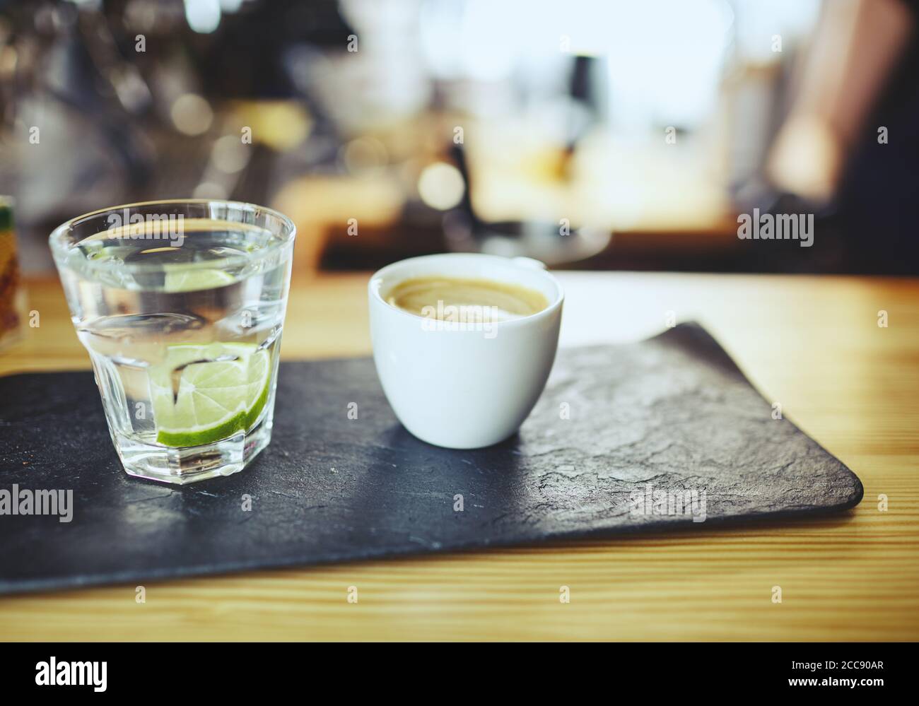 Verschwommenes Bild von Steinplatte mit Tasse Kaffee und Wasser in einem Glas mit Kalk auf der Theke.Kaffeepause Stockfoto