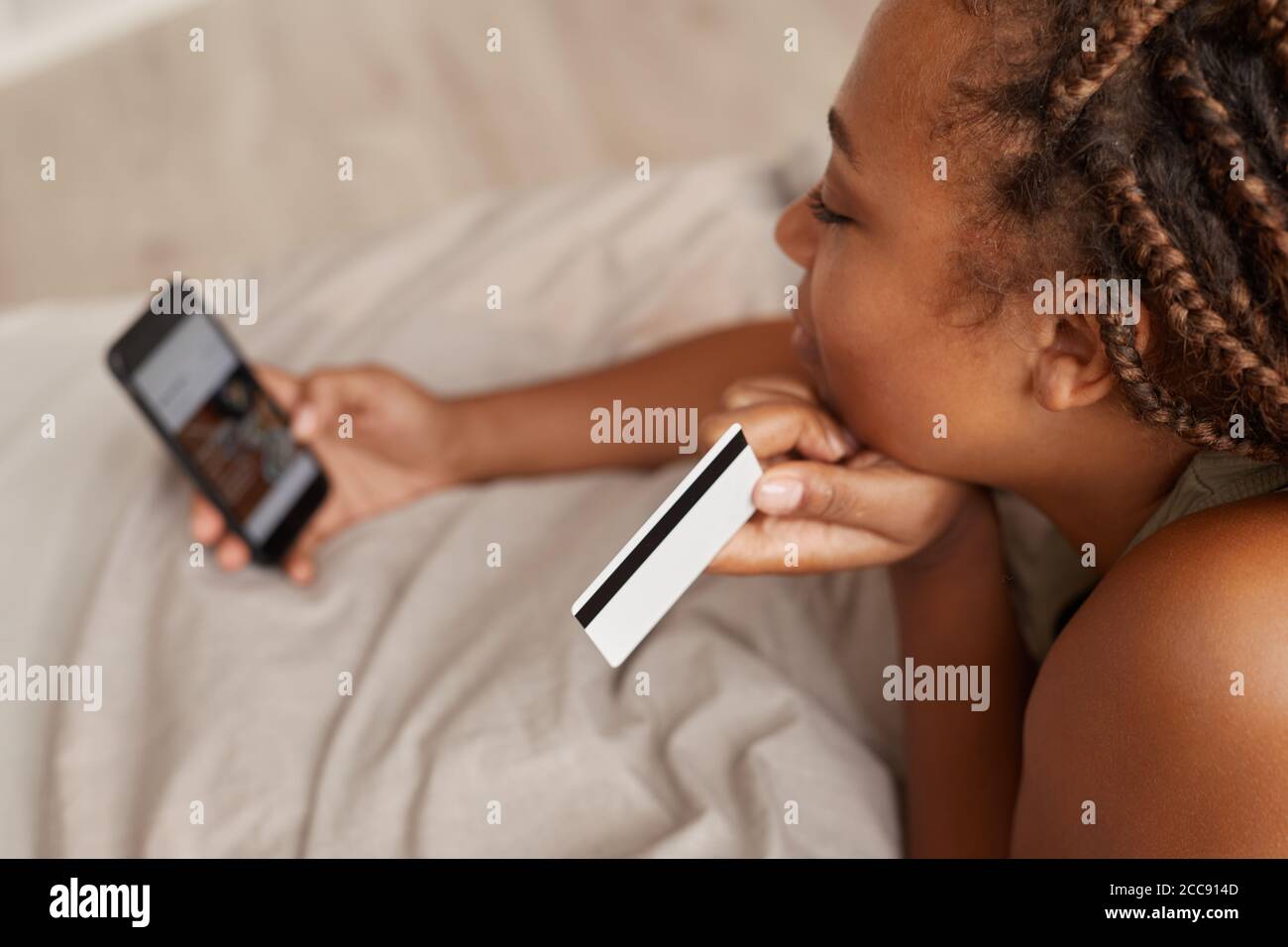 Nahaufnahme einer Frau, die mit ihrer Kreditkarte auf dem bezahlt Telefon während sie in ihrem Bett lag Stockfoto