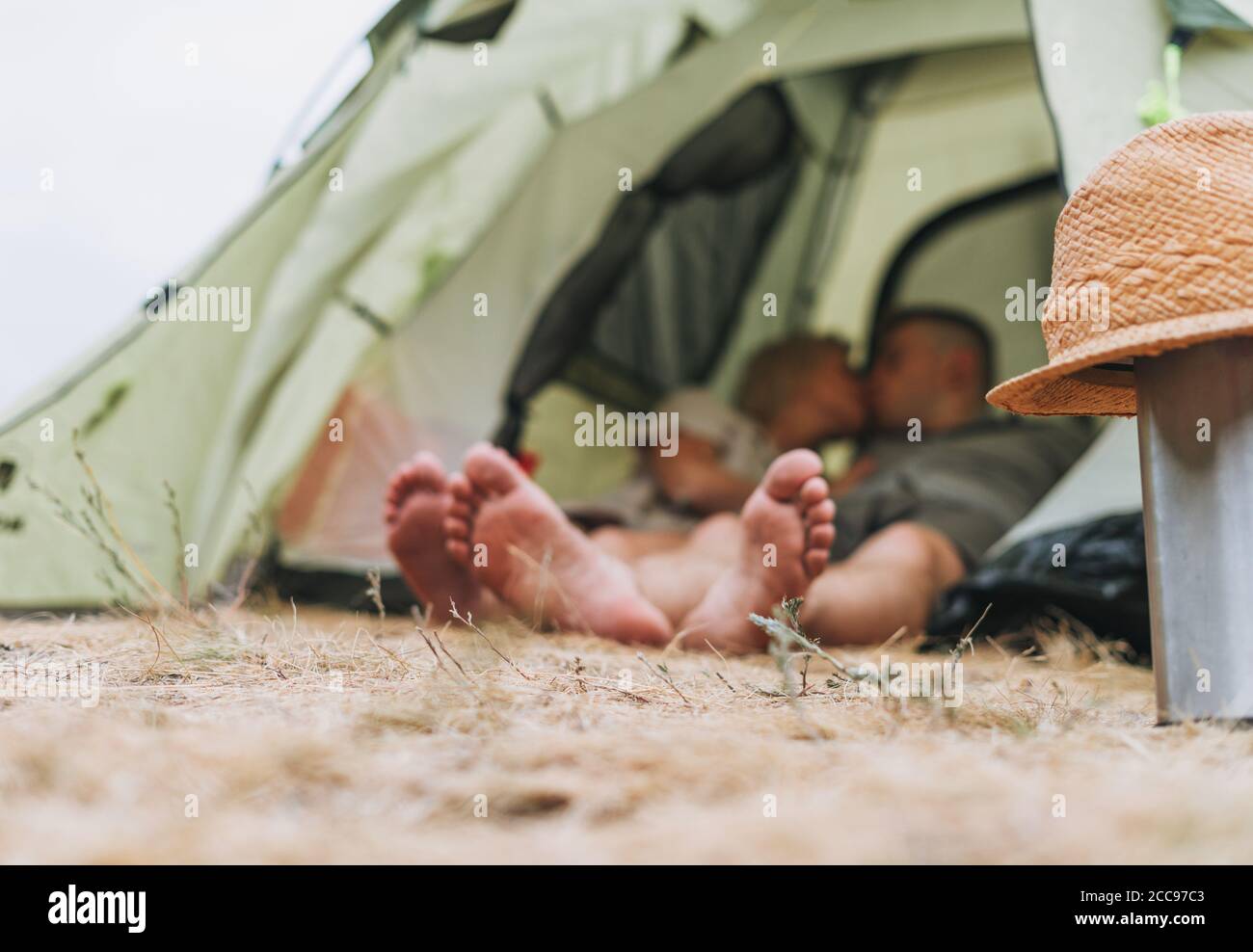 Glückliche junge Paar Reisende in lässigen Outfits küssen im Zelt. Konzentrieren Sie sich auf Strohhut. Lokaler Tourismus, Wochenend-Trip-Konzept Stockfoto