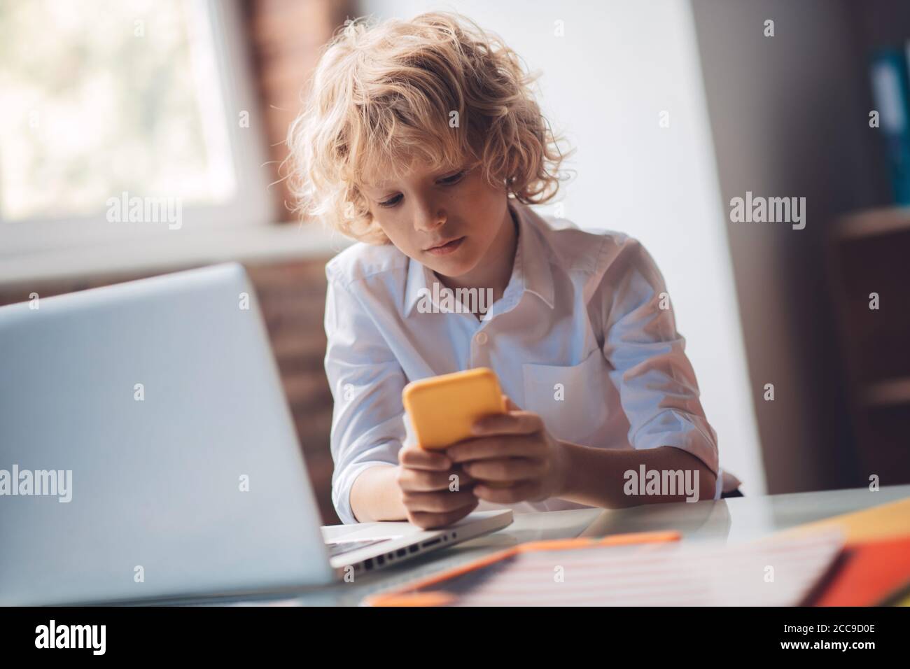 Cute blonde junge hält sein Smartphone und SMS Stockfoto