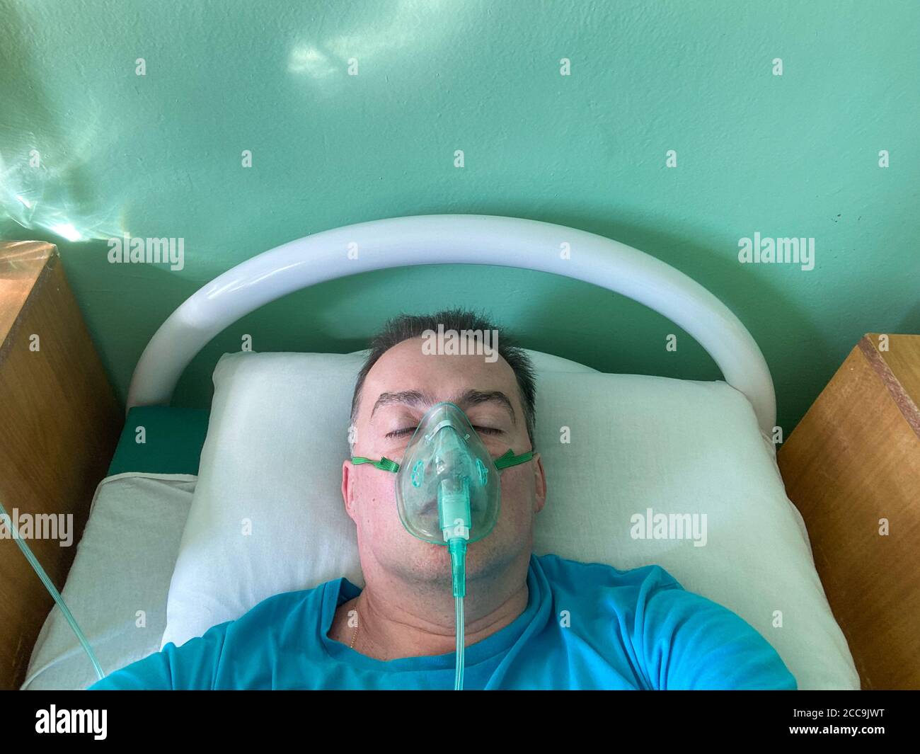 Patient in einer Atemsauerstoffmaske liegt in einem Krankenhaus auf einem Bett. Behandlung von Coronavirus und Lungenentzündung Konzept. Speicherplatz kopieren Stockfoto