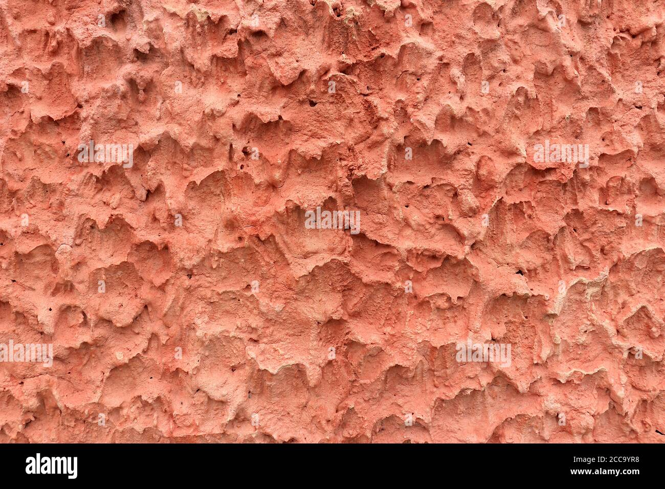 Die Oberfläche der Zementwand macht sie rau. Es ist eine ungewöhnliche Textur mit einer rötlich-rosa Farbe. Stockfoto