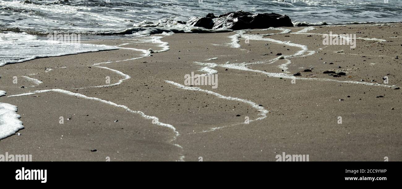 Weiße Schaumstofflinien am Strand mit dem Meer und Felsen Stockfoto