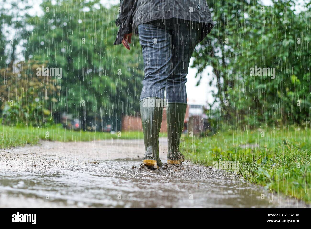 Niedriger Winkel, Rückansicht der Frau (unterer Abschnitt), die Gummistiefel und Gummistiefel trägt, bei starkem Regen, die von der Kamera weg auf dem schlammigen UK-Pfad geht. Stockfoto