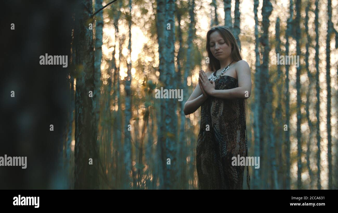 Gebet oder magisches Ritual im Wald. Junge kaukasische Frau, die im Wald meditiert oder betet. Zeitlupe und Kopierbereich. Hochwertige Fotos Stockfoto