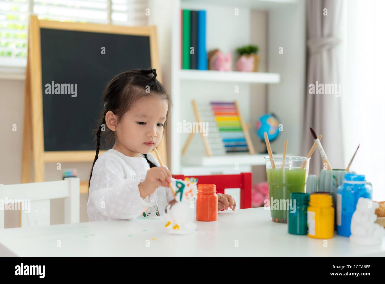 Asiatische Kindergarten Schule Mädchen Malerei Gips Puppe mit Acryl Wasser Farbe Farbe im Wohnzimmer zu Hause. Homeschooling und Fernunterricht. Stockfoto