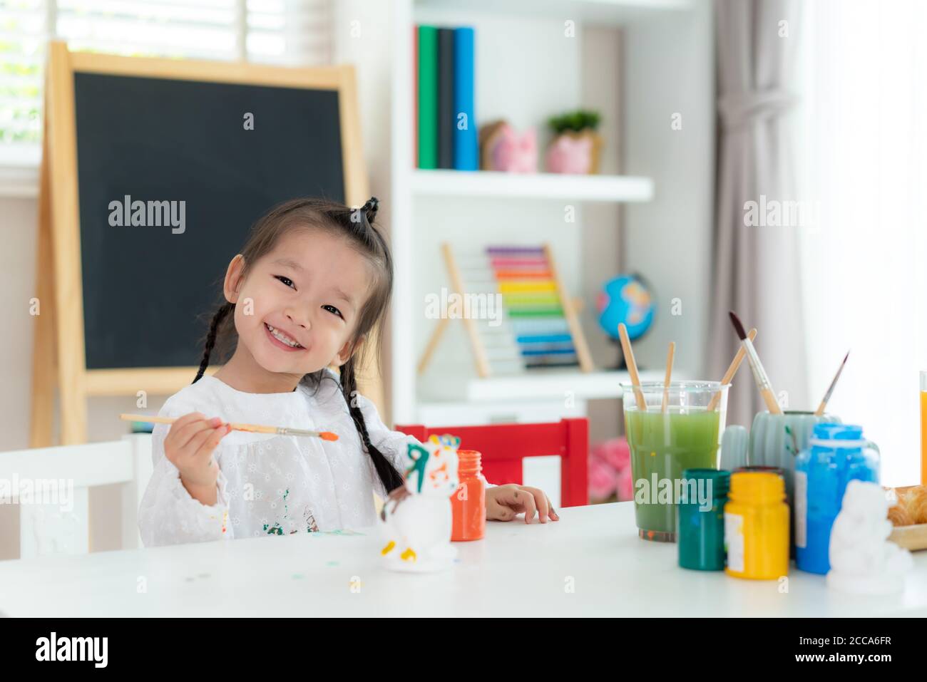 Asiatische Kindergarten Schule Mädchen Malerei Gips Puppe mit Acryl Aquarell und lächelnd Blick auf Kamera im Wohnzimmer zu Hause. Homeschoolin Stockfoto