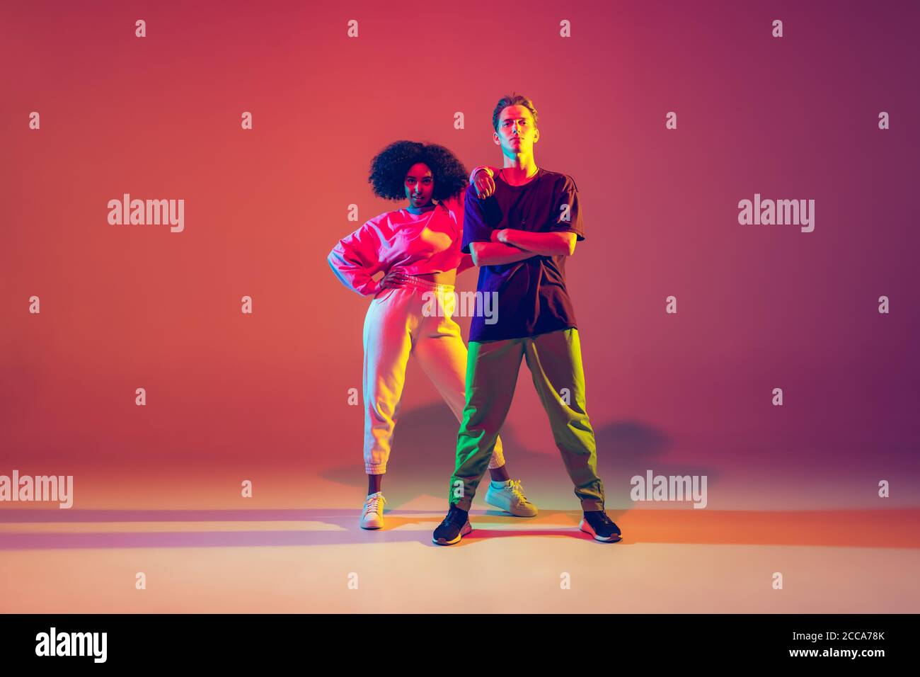 Sommer. Stilvoller Mann und Frau tanzen Hip-Hop in hellen Kleidern auf grünem Hintergrund in der Tanzhalle in Neonlicht. Jugendkultur, Bewegung, Stil und Mode, Action. Modisches Porträt. Stockfoto