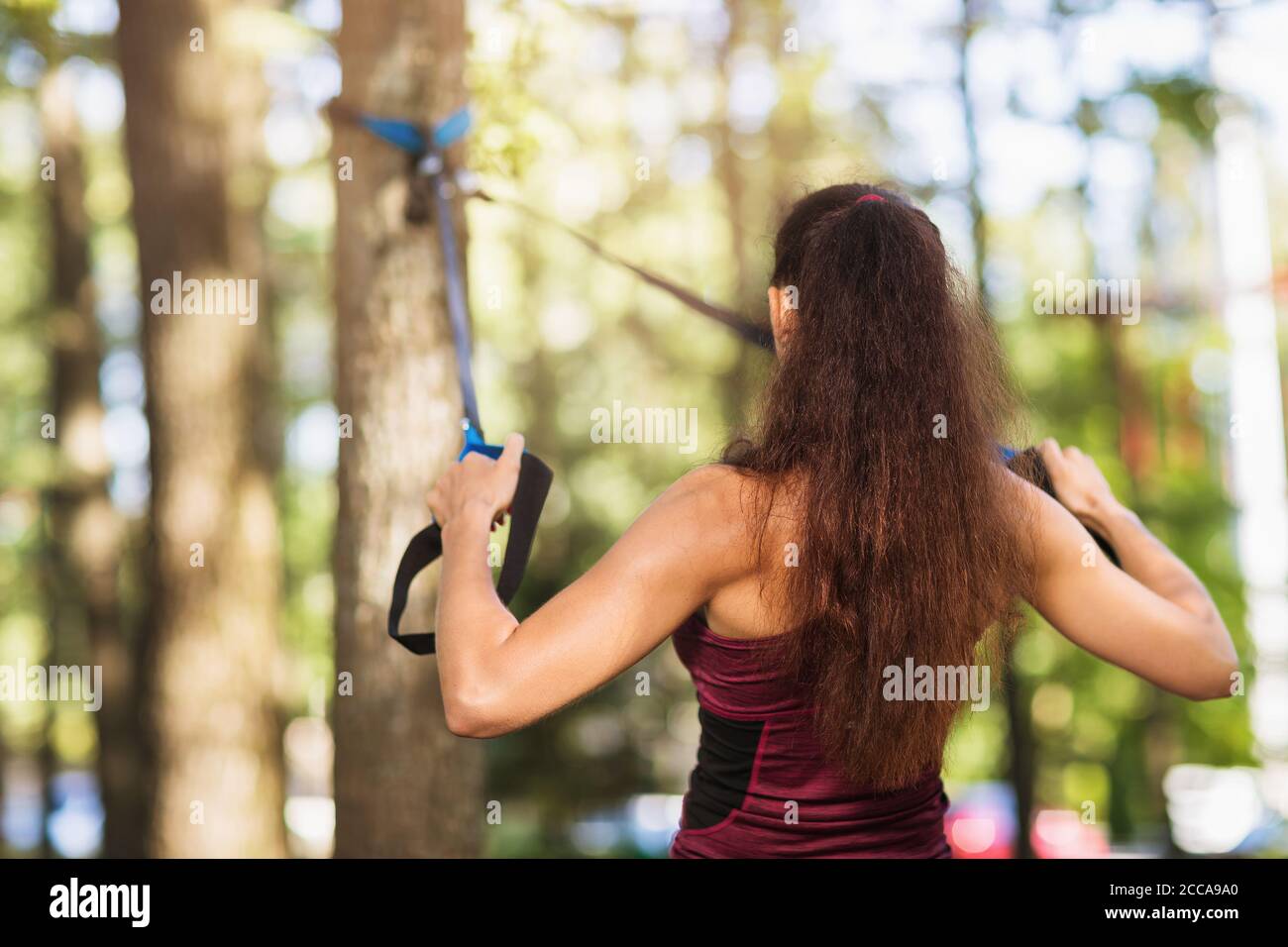Junge Frau führt eine Übung, um die Muskeln des Rückens mit Fitness-Gurte an einem Baum im Park befestigt trainieren. Gesundes Lifestyle-Konzept Stockfoto