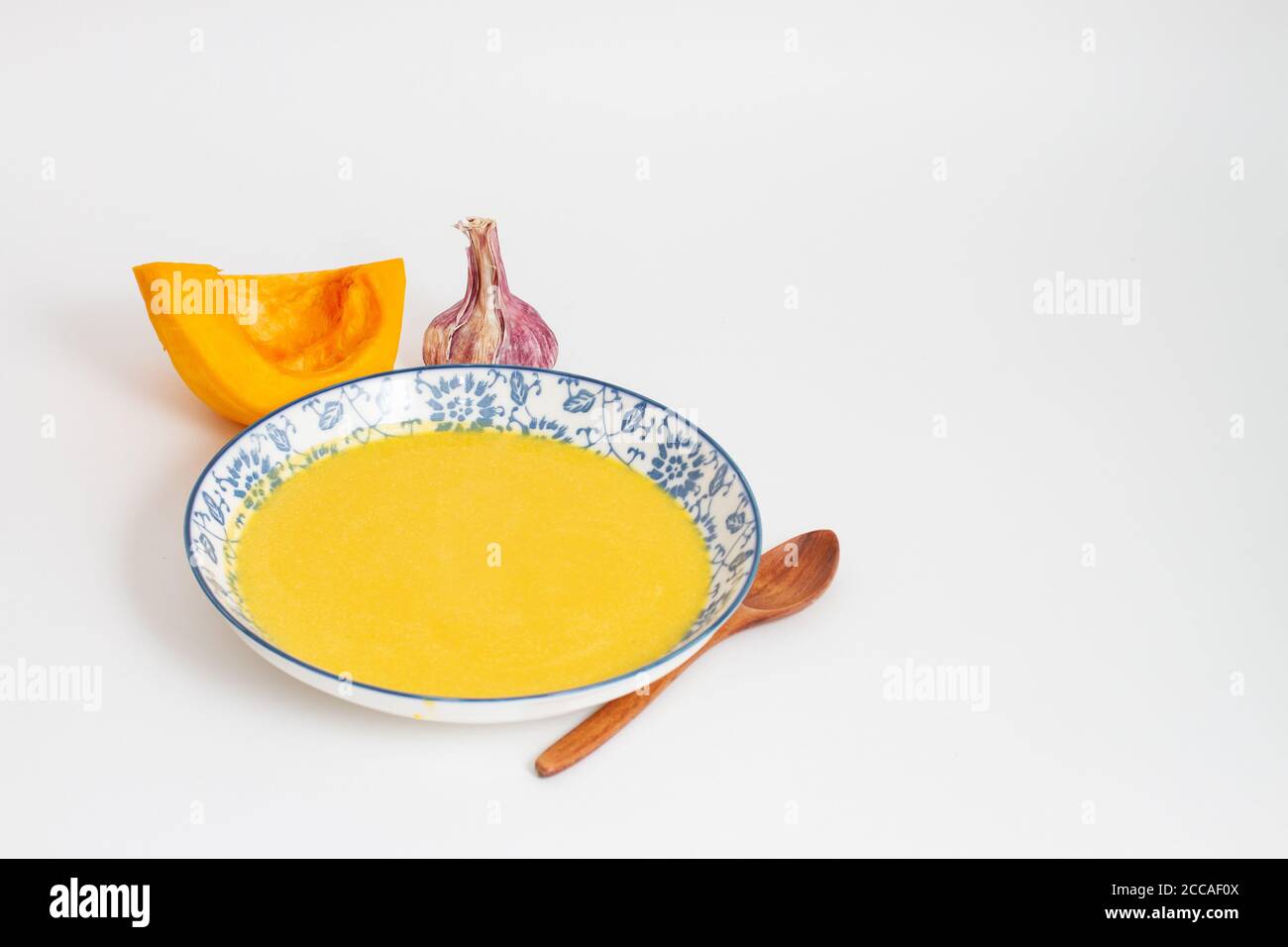 Kürbiscremesuppe in Schüssel auf weißem Hintergrund. Speicherplatz kopieren. Eine Scheibe Kürbis, Knoblauch und einen Holzlöffel auf dem Tisch Stockfoto