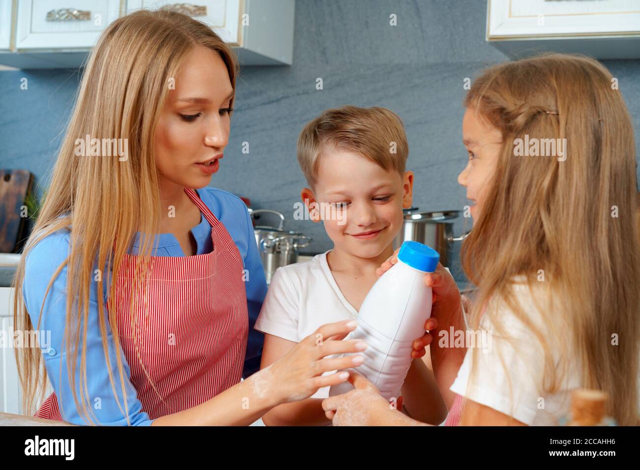 Cute blonde Kinder helfen ihre Mutter in der Küche vorbei Flasche Milch Stockfoto