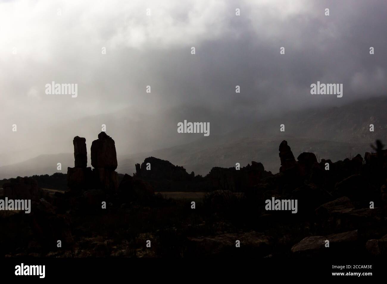 Dunstiges Licht bricht durch die dicken Regenwolken in den Cederberg Bergen in Südafrika, mit den Silhouetten des seltsamen Sandstein-Rock-Formats Stockfoto