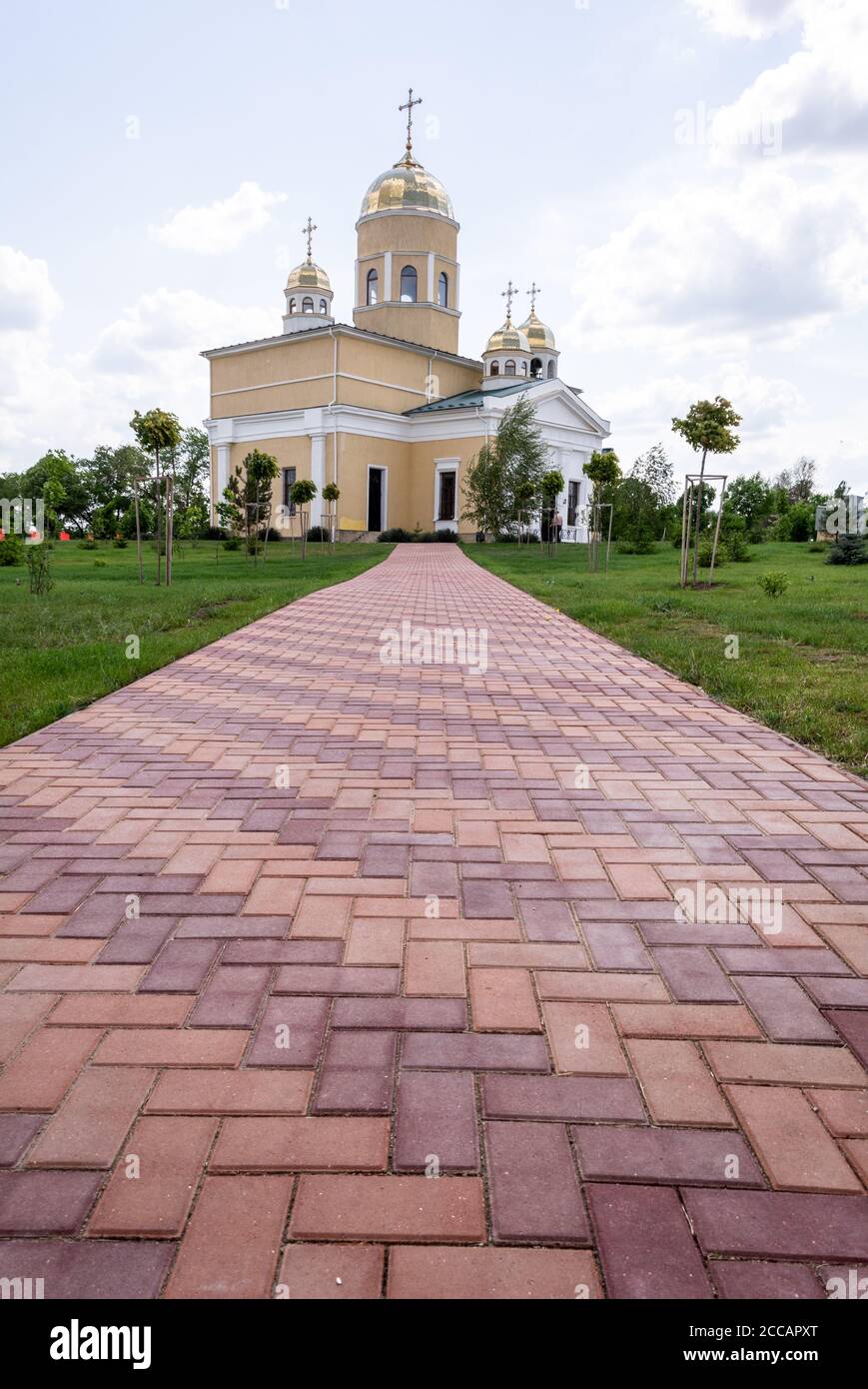 Moldawien, Bender - 18. Mai 2019: Eine mit roten Pflasterplatten gepflasterte Straße führt zu einer Kirche am Horizont gegen einen blauen Himmel mit Wolken. Stockfoto