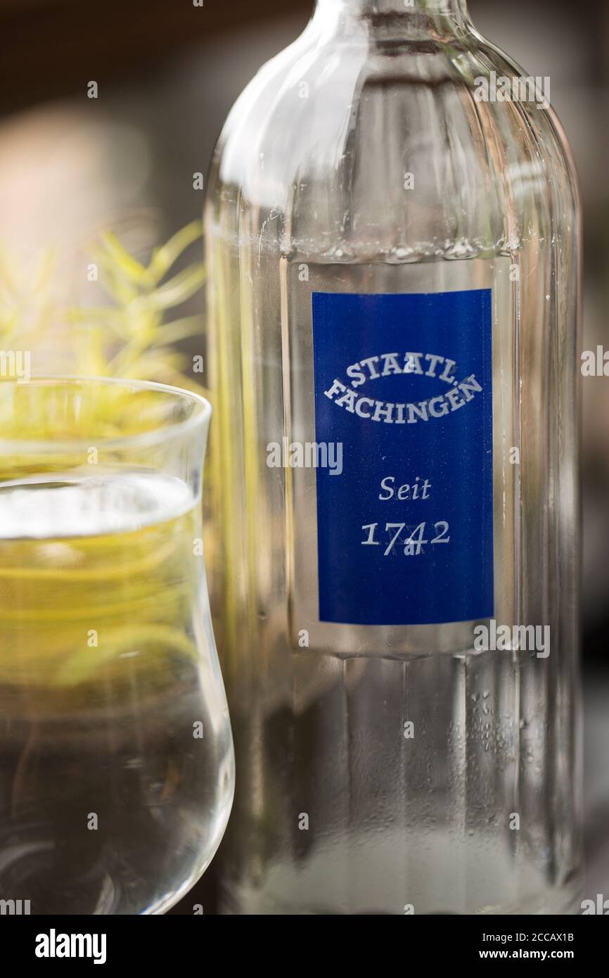 Eine Flasche Mineralwasser der deutschen Staatl. Fachingen auf einem Tisch neben einem Glas. Stockfoto