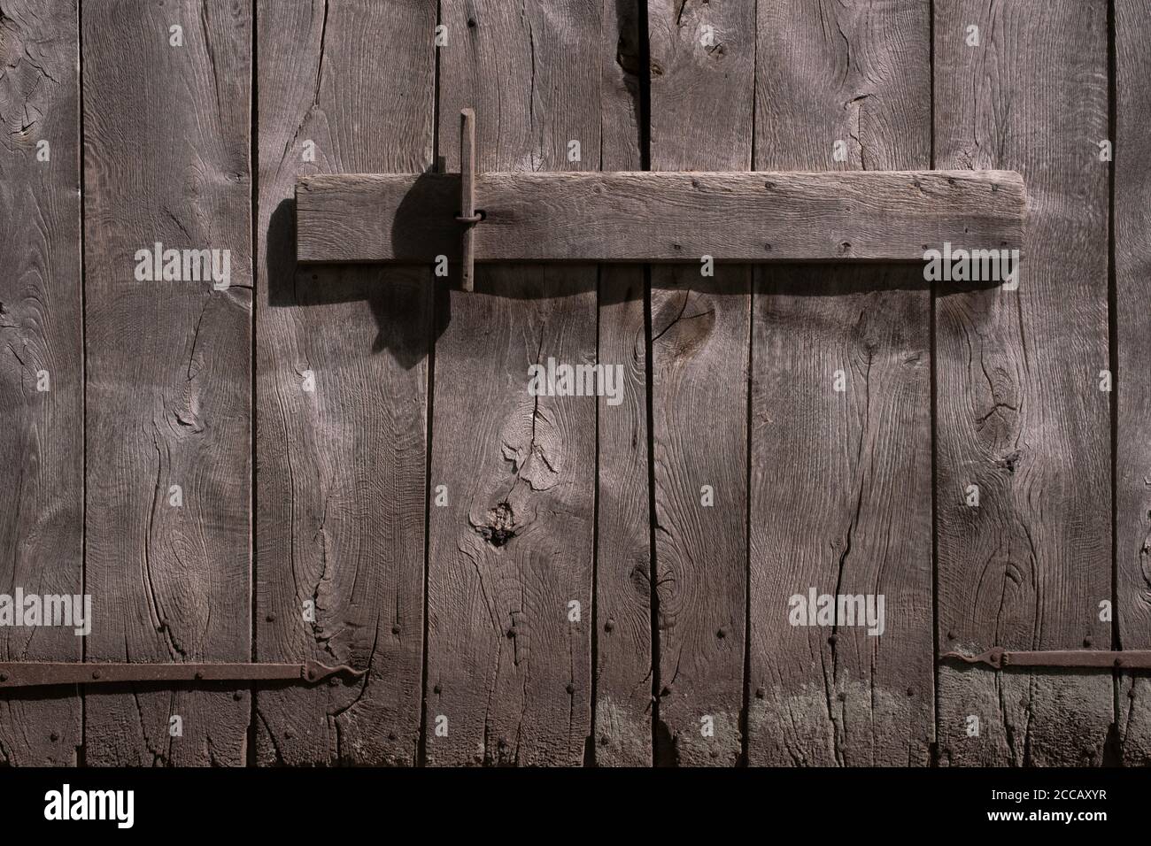 Alte verfallene grau-braune hölzerne Scheunentüren mit rostigen Metallscharnieren, geschlossen mit einem horizontalen Holzbalken Stockfoto